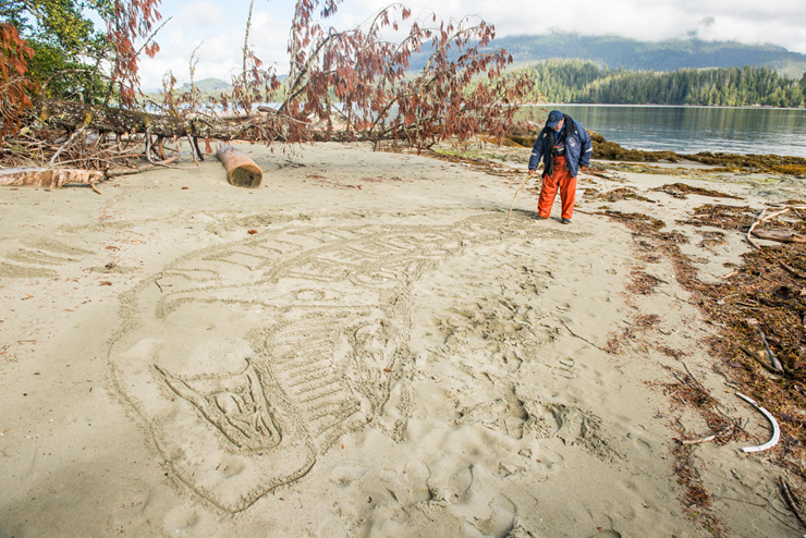 Image: The Tseshaht Beach Keepers help Parks Canada to manage environmental and visitor safety in the Broken Group Islands. Here one of the Beach Keepers creates a traditional whale drawing in the sand. Pacific Rim National Park Reserve.
